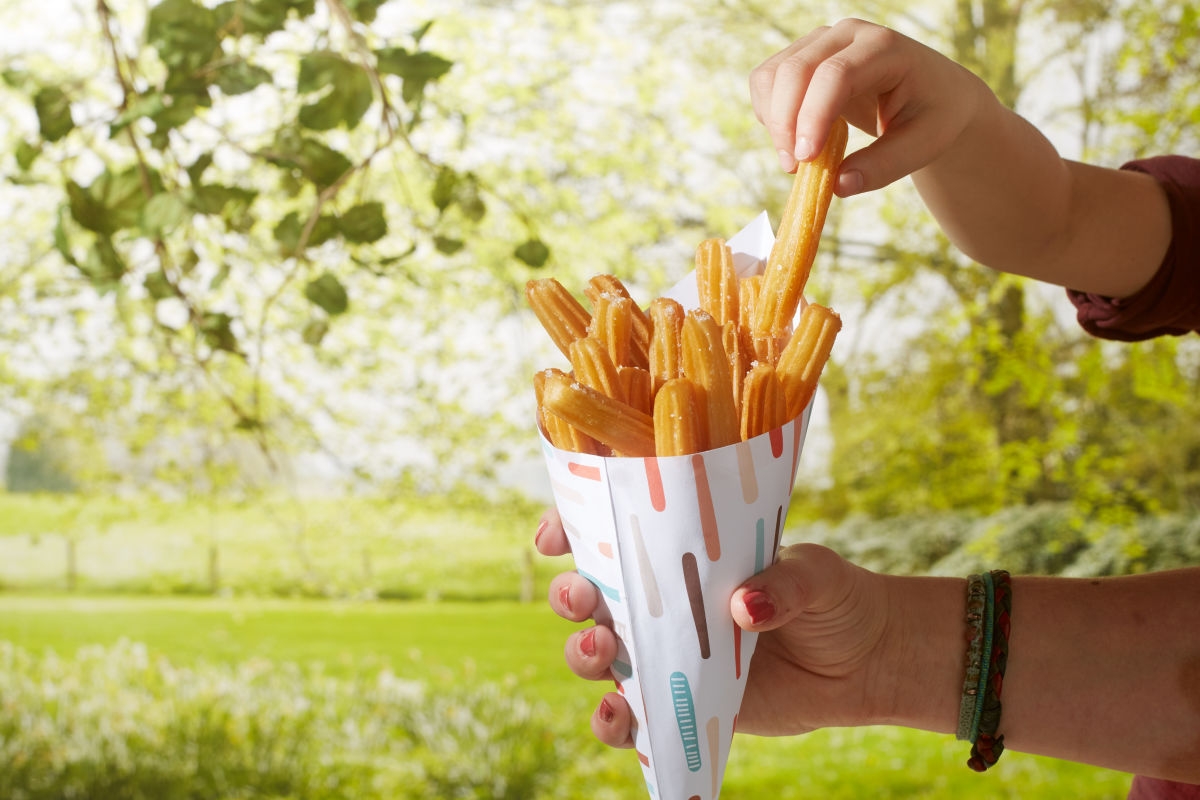 Churros vor grünem Hintergrund in einer Papiertüte serviert