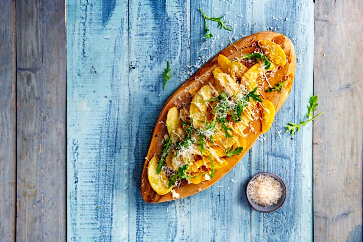 anwendung dünner kartoffelspalten auf holzbrett und blauem tisch als snack mit toppings