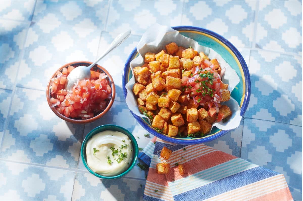 Patatas bravas angerichtet in einer Schale neben salsa und aioli dips