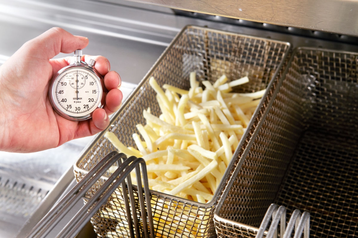 Pommes in der Fritteuse mit Stoppuhr im Vordergrund zur Zeitmessung des Frittiervorgangs